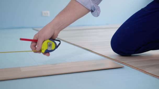 Renovação apartamento ou casa, closeup mãos homem com uma fita métrica mede o comprimento do laminado antes de instalar em folhas de isopor — Vídeo de Stock