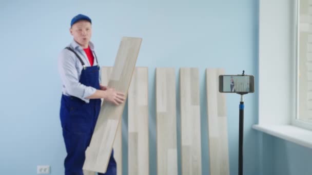 Handyman takes video blog during laying the laminate on a mobile phone, man in work suit and cap use gadget during a conversation — Stock Video