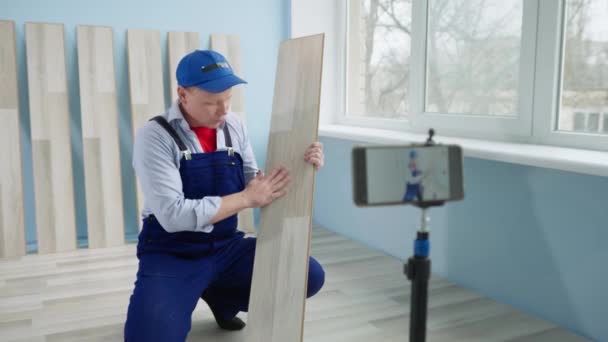 Blog de vídeo ao colocar o laminado, homem com placa em mãos fazendo registro no celular durante o reparo em uma nova casa — Vídeo de Stock