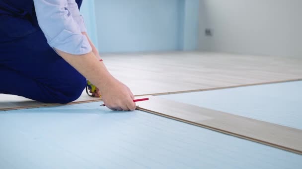 Man with a pencil and tape measure makes measurements of the board before installing on styrofoam sheets, laying laminate flooring during renovation — Stock Video