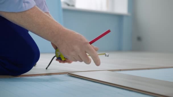 Mãos do trabalhador com lápis e fita métrica faz medições de laminado antes de instalar no poliestireno expandido, renovação na sala — Vídeo de Stock