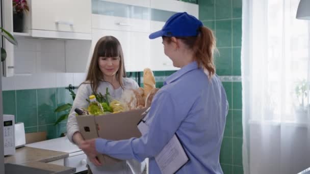 Интернет-магазин, женщина-курьер доставляет картон домой к счастливой девушке, заказывающей еду из интернет-магазина, находясь дома — стоковое видео
