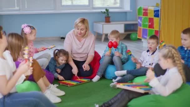 Gyermekek élvezik a zeneórát az osztályteremben női tanár, gyerekek Down-szindróma és egészséges gyerekek játszanak maracas, xilofonok és harangok — Stock videók