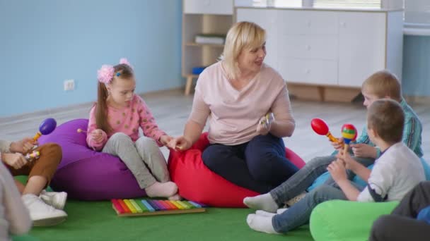 Bambini con sindrome di Down in lezione di musica, insegnante di musica femminile suona strumenti musicali con i bambini seduti su sedie multicolore sacchetto di fagioli — Video Stock