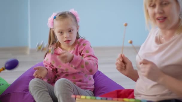 Jouets d'apprentissage, petite fille avec le syndrome du duvet avec des cloches jouer avec une femme avec un xylophone pendant la leçon de musique assis sur des chaises de sac de haricot — Video