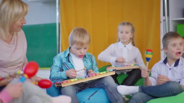 Barn njuter musik lektion i klassrummet med sin lärare, pojkar med ner syndrom och flicka spela på maracas och xylophones — Stockvideo