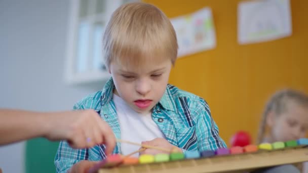 Учитель учит мальчика с синдромом Дауна играть на ксилофоне, ребенок с инвалидностью дает пять педагогу во время урока музыки — стоковое видео
