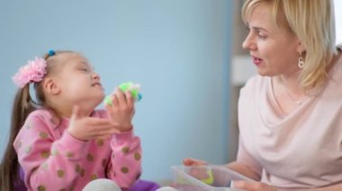 Dokunsal oyuncaklarla Down sendromlu çocuk öğretmenle eğleniyor, küçük kız zevk ve alkış alıyor.