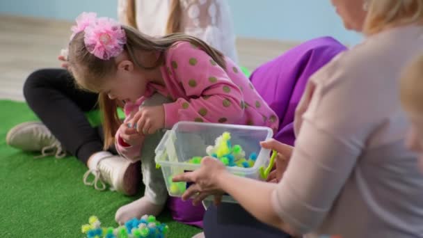 Kind mit Behinderung verbringt Zeit mit Lehrerin auf Sitzsäcken sitzend, kleines Mädchen mit Down-Syndrom spielt mit Spielzeug — Stockvideo
