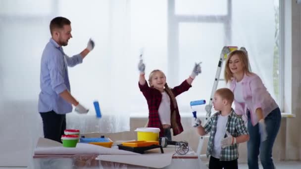 Rodzina mężczyzna kobieta i chłopiec z zespołem Downa z siostrą razem radować się z nowego remontu w mieszkaniu i zabawy taniec z rolkami w ich rękach — Wideo stockowe