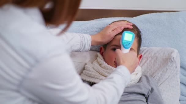 L enfant présentant les symptômes d'une maladie soignante parent mâle mesure la température élevée en Celsius avec thermomètre sans contact pendant la pandémie due au coronavirus — Video