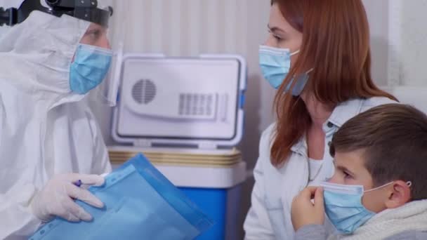 Koruyucu giysili kadın doktor, hastalık belirtileri gösteren çocuk sağlığı konusunda anne babaya danışıyor — Stok video