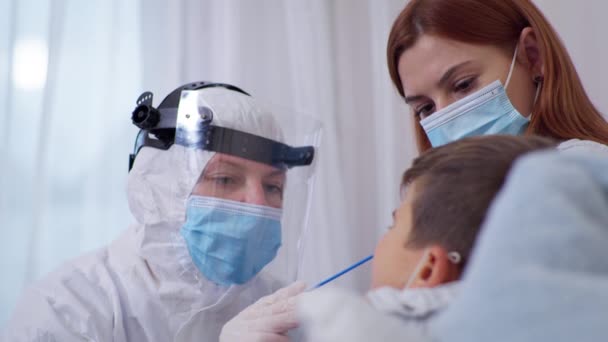 Manliga barn med dålig hälsa testas för coronavirus till kvinnlig läkare i skyddsdräkt och mask för att skydda mot virus och infektion — Stockvideo