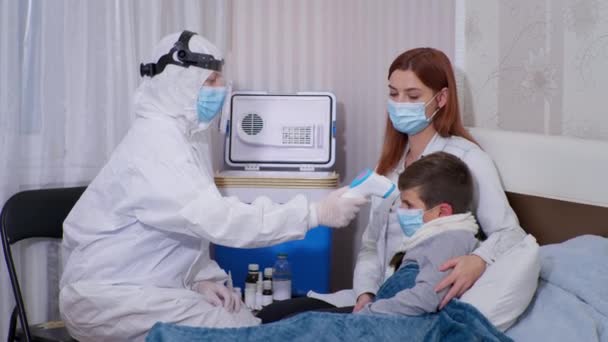 Ärztin im Schutzanzug untersucht ungesunden Jungen mit Krankheitssymptomen, misst Körpertemperatur mit berührungslosem Thermometer — Stockvideo