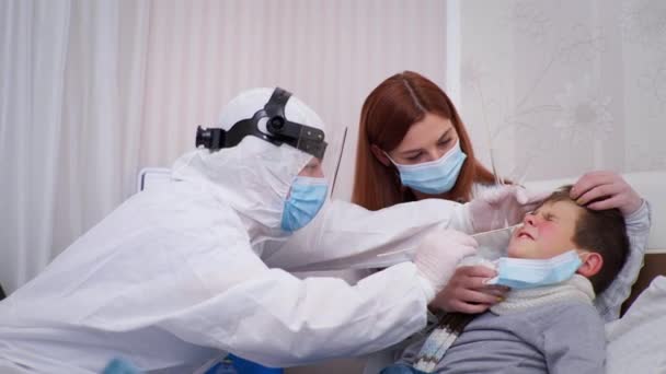 Zdravotnický pracovník v ochranném obleku vyšetřuje mužského pacienta a bere virus a infekční test, milující matka se stará o syna nezdravé zdraví — Stock video