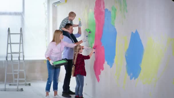 Familie mit männlichem Kind mit Down-Syndrom um den Hals ihres Vaters und ihrer älteren Schwester arbeiten gerne zusammen und streichen Wände der neuen Wohnung — Stockvideo