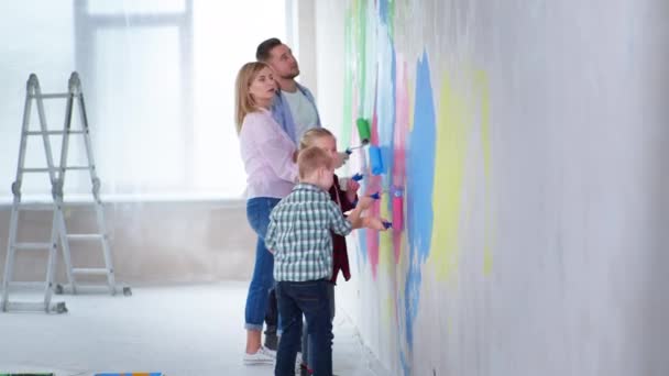 Άνδρες και γυναίκες γονείς με σύνδρομο down αγόρι και κορίτσι ζωγραφίσει τοίχο με χρωματιστά χρώματα σε εσωτερικούς χώρους κατά τη διάρκεια της ανακαίνισης — Αρχείο Βίντεο