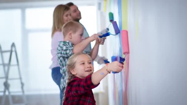 Menina com rolo rosa nas mãos pinta paredes fundo de famílias de mãe e pai e irmão com síndrome de down durante o trabalho de acabamento dentro de casa — Vídeo de Stock