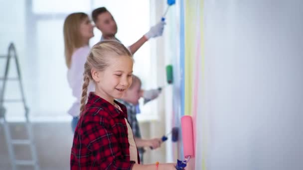Lány rózsaszín görgő a kezében festéket falak bátyja down szindróma és a szülők a háttérben a ház felújítása során — Stock videók