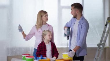 Erkek olarak kadın çocuk gözetiminde olan kadın, boya ile kovayı karıştırıyor. İnşaat matkabını evde onarım sırasında kullanıyor.
