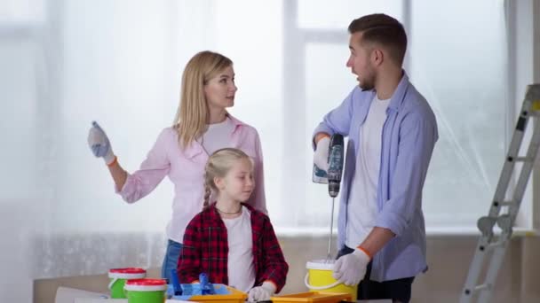 Frau mit Kind beobachtet, wie Mann Pigment mit Farbe im Eimer mit Baubohrer in Wohnung bei Renovierung mischt — Stockvideo