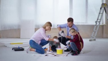 Anne kız ve erkek kardeşi Down sendromlu. Baba pigmenti kovadaki boyayla karıştırıyor. Kapalı alanda inşaat matkabı kullanıyor.