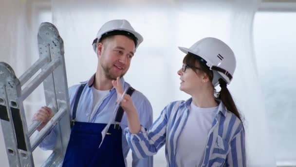 Trabajo en equipo en sombreros duros con una escalera y una combinación de colores para pintar paredes en interiores — Vídeos de Stock