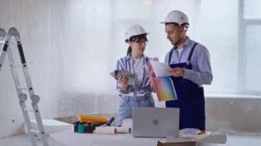 Renk örneğine sahip kadın tasarımcı ve inşaat alanındaki duvar boyasını seçen kasklı erkek inşaatçı.