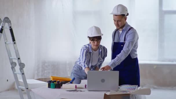 건축 현장에서 벽에 칠 할 페인트를 고르는 안전 헬멧을 쓰고 있는 여자 디자이너와 남자 건축가 — 비디오