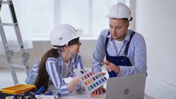 보호용 헬멧과 색상을 손에 들고 있는 직업적 인 남녀 건축가들은 개조를 위한 준비 로새 로운 벽의 설계에 관해 이야기 한다 — 비디오