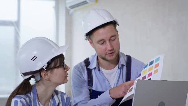 Ritratto di lavoratori professionisti uomo e donna in caschi protettivi e campione di colore nelle loro mani discutere la progettazione di nuove pareti — Video Stock