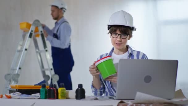 Diseñador femenino utiliza las tecnologías modernas se comunica con el cliente a través de vídeo en el ordenador portátil y discute el color de la pintura para las paredes de la paleta — Vídeos de Stock