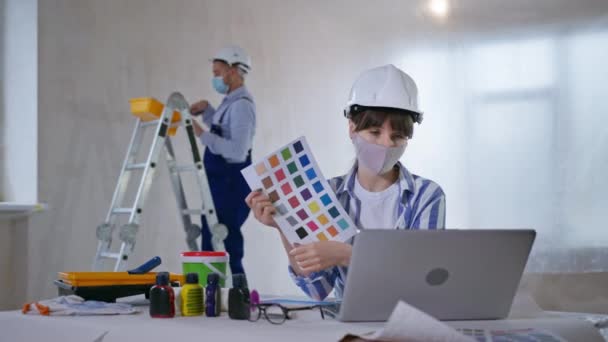 Remont domu w kwarantannie, kobieta nosząca maskę ochronną na twarzy omawia ściany projektowe z klientami wybierającymi kolor z palety z linku wideo na laptopie — Wideo stockowe