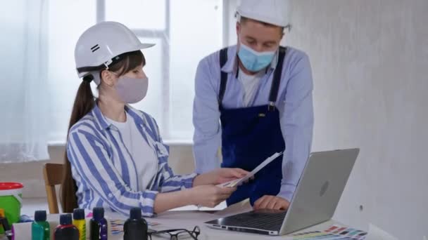 Friendly team of specialists, man and woman wearing masks on their faces to protect against virus and infection, discuss design of walls on color palette — Stock Video