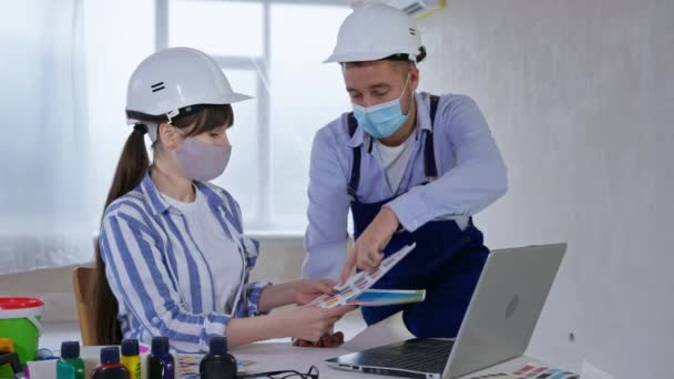 Builders male and female wearing masks on faces to protect against virus and infection discuss design of walls on color palette during renovation indoors — Stock Video
