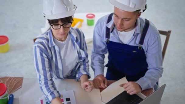 Trabajadores de la construcción masculinos y femeninos discutiendo nuevas renovaciones y eligiendo el color de pared en la paleta — Vídeos de Stock