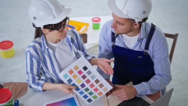 Workers man and woman in safety helmets doing interior design and choosing new wall paint from color scheme, repairs — Stock Video