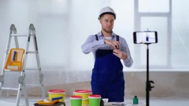 Miğferli adam duvarlar için boya yapmaktan bahsediyor ve canlı yayın sırasında akıllı telefondan kamerayı işaret ediyor.