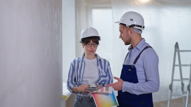 Professionals woman and man in helmets are doing repairs indoors and choosing wall design from color scheme at construction site — Stock Video