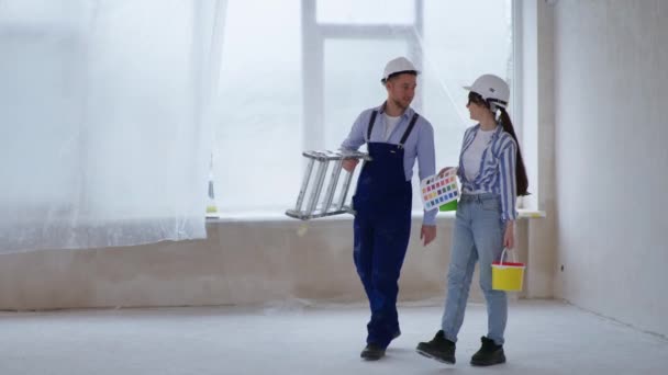Construtor homem feliz com escada rolante e jovem designer com pintura e paleta de cores nas mãos discutir renovação dentro de casa — Vídeo de Stock