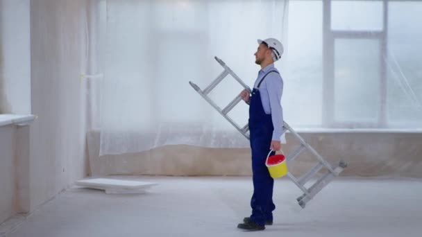 Εργάτης οικοδομών με βάψιμο και βαφή στο χέρι προετοιμάζεται για τη ζωγραφική και ξετυλίγει σκάλα — Αρχείο Βίντεο
