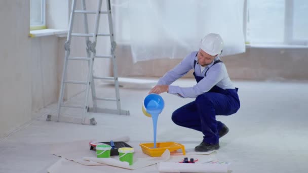 Uomo in abiti da lavoro e cappuccio versa colorante blu in vassoio di vernice per dipingere pareti durante la ristrutturazione — Video Stock