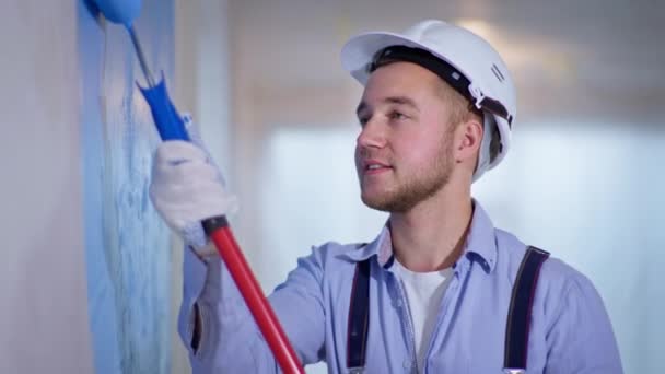 Pintor hombre con rodillo de construcción en sus manos pinta paredes durante el diseño y la renovación en interiores en el sitio de construcción — Vídeos de Stock