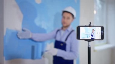 Genç adam akıllı telefon kamerasıyla işi nasıl bitireceğini kaydediyor ve evin tadilatı sırasında duvarları silindirle boyuyor.