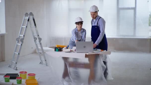 Desainer perempuan dengan pekerja bangunan dalam helm keselamatan membahas cat untuk dinding memilih bayangan dari warna swatch selama renovasi dalam ruangan — Stok Video
