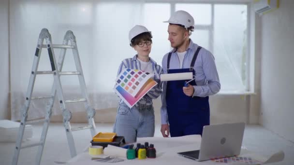 Designerin mit Farbpalette und professioneller männlicher Bauarbeiter mit Walze zum Bemalen der Wände in der Hand wählen Farbe für Malraum — Stockvideo