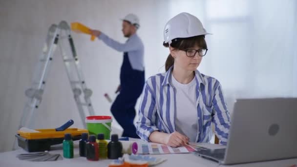 Desainer wanita bersukacita karena pilihan warna cat untuk dinding dengan palet warna di tangan yang duduk di meja dengan laptop — Stok Video