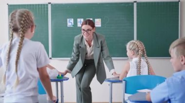 Tahtaya yakın öğretmen ders veriyor, okul çocukları pedagog dinliyor ve doğru cevabı bilerek ellerini kaldırıyor. Kalk ve sınıfta cevap ver.
