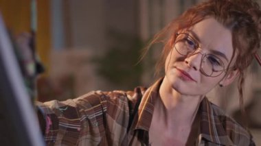 Ressam resim çizer, yakın plan, gözlüklü yakışıklı kız kirli ellerle resim yapar, stüdyoda fırçayla resim yapar.