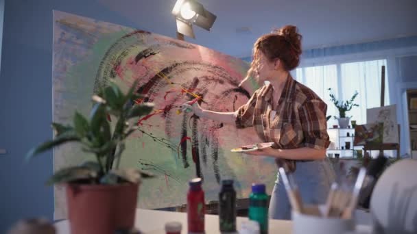 Δημιουργικός καλλιτέχνης χρησιμοποιεί ενεργά ένα πινέλο, ενώ η δημιουργία ενός πίνακα σε μεγάλο καμβά, κομψό κορίτσι κατά τη διάρκεια χόμπι στο στούντιο — Αρχείο Βίντεο